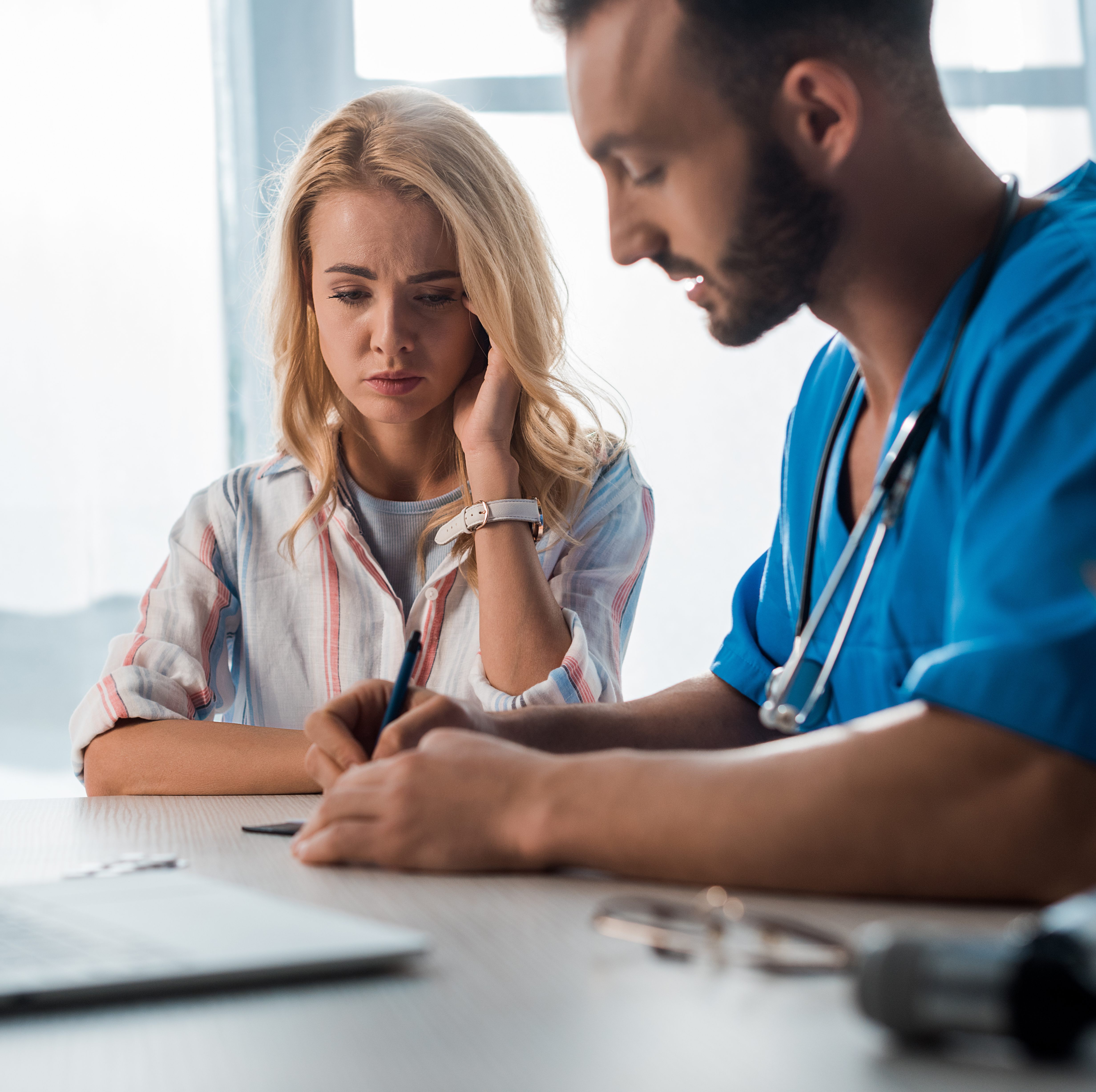 selective focus of sad woman near doctor writing prescription